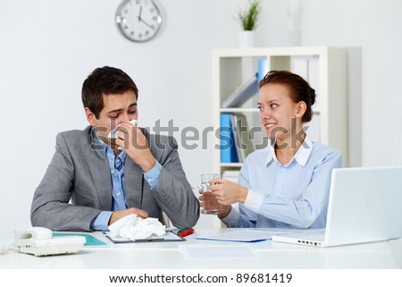 Image of businessman sneezing while his partner giving him tablets and water in office