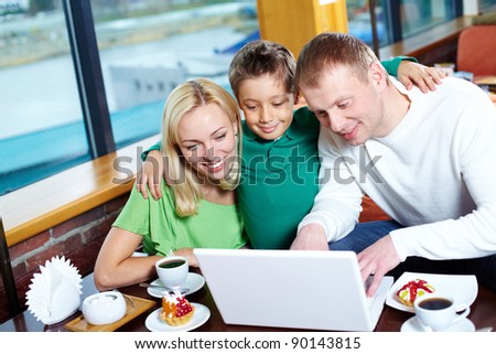 Image of happy family looking at laptop screen in cafe