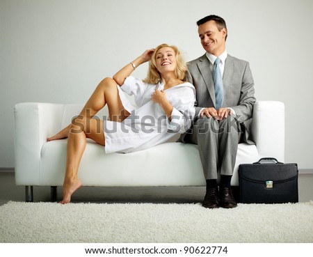 Photo of man in suit sitting on sofa and looking at seductive woman near by