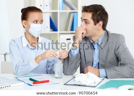 Image of sick businessman with tissue looking at his colleague in mask dissolving solution for him in office