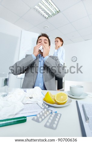 Image of businessman sneezing while his partner on background looking at him with fright in office