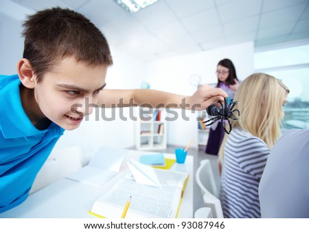 Evil lad holding black spider and going to frighten his classmates at lesson