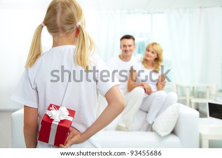 Back view of daughter hiding giftbox while looking at her parents