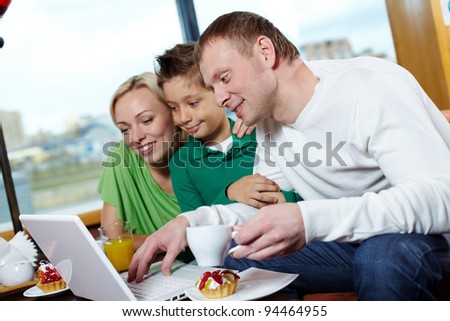 Happy family of three using a laptop while being at a cafe