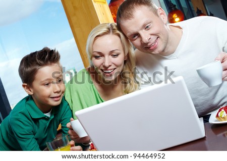 Happy family of three using a laptop while having lunch