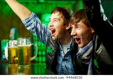 Happy men shouting while watching football match broadcast in pub