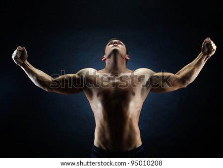 Handsome young man with his hands raised up victoriously against black background