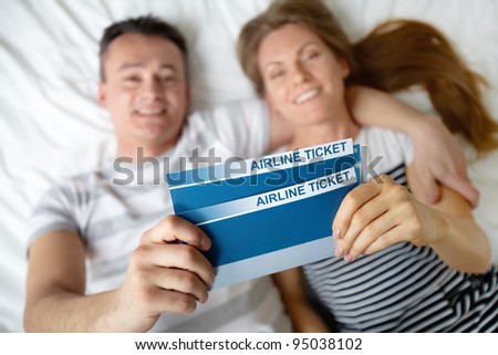 Happy young couple lying on bed with air tickets in hands