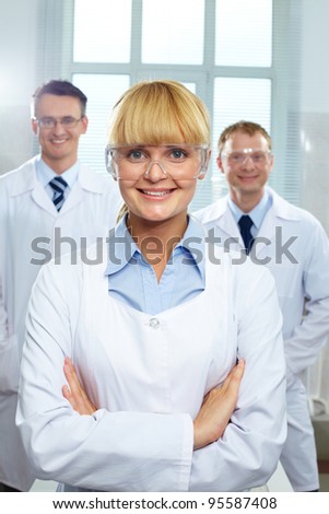 Pretty female reader looking at camera and smiling, her colleagues standing behind