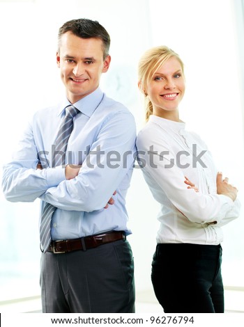 Two business people standing back to back and smiling at camera
