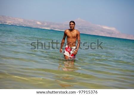 Young man looking at camera while walking in water on southern resort