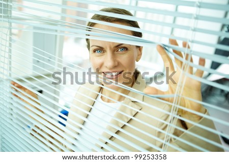 Confident business woman sliding apart blinds to see better what is going outside