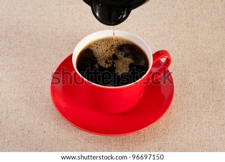 Red coffee cup being filled with black coffee. Last drops dripping out of the coffee pot.