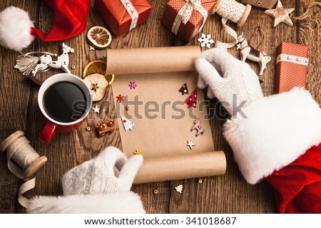 Santa Claus with gifts and wish list on wooden table