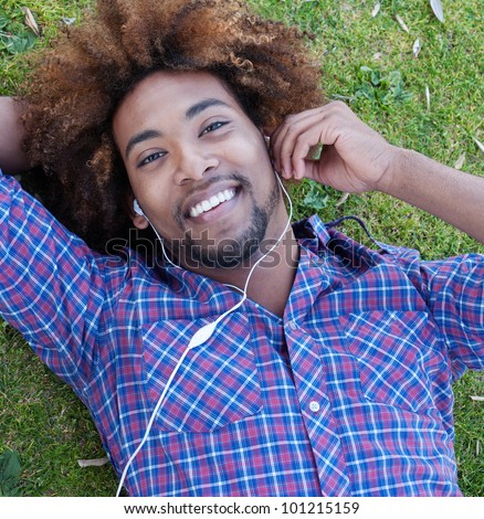 young, happy african american male lying in grass listening to music
