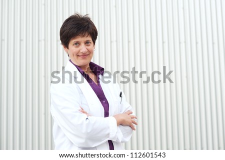 Smiling mature professional woman dressed in lab coat standing outside