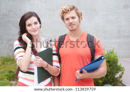 Happy pair of students holding notebooks outdoors