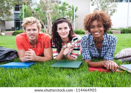 group of happy college students lying in the grass with notebooks