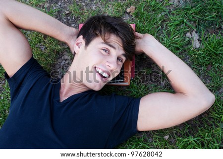 Young male student lying on grass with books