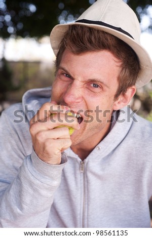 portrait of a young man eating apple outside