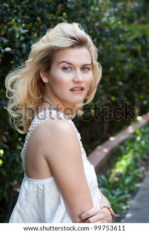 close-up portrait of beautiful young blonde woman in white blouse at park holding her neck