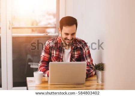 Successful entrepreneur smiling in satisfaction as he checks information on his laptop computer while working in a home office.