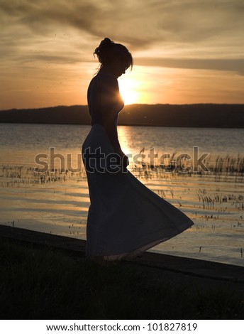Young, slim lady dances alone at the beach, sunset