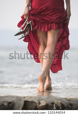 Sexy red dressed woman walks on wet stone next to sea