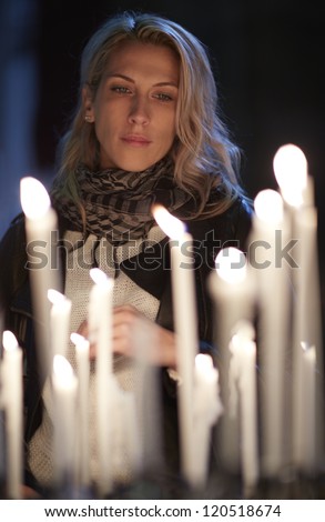 Beautiful woman prays, stands behind candles