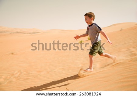 Young boy runs down in desert sand