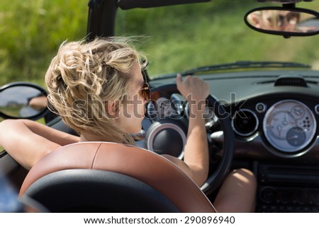 Blonde woman drives open top car, in summer sunshine