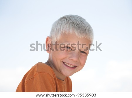 Jolly little boy laughs, orange shirt, blue sky