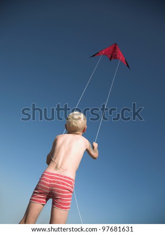 Young blonde boy plays with red kite