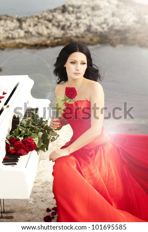 beautiful slim bride in red wedding dress playing grand piano on sunset beach. Fashion romantic stylish arabian young girl musician with long glossy healthy hair. Spring - summer