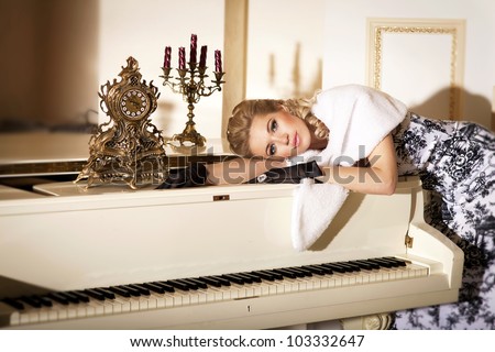 alluring blond woman pianist with grand piano in luxury hotel. Stylish rich slim girl in gloves elegant dress and fur with healthy glossy hair at villa apartment. Lady musician with diamond jewelry