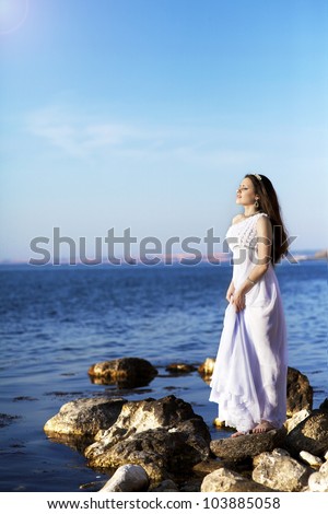 beautiful slim bride in wedding dress on sunset beach near sea. young woman in Greek  goddess style with diamond tiara and jewelery. Fashion stylish romantic girl with glossy hair. Spring - summer