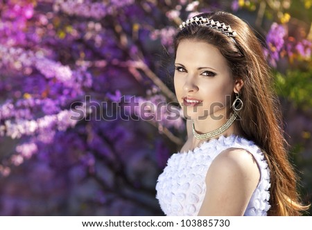 beautiful slim bride in luxury dress in park on sunset near blossom flowers in wedding day. young woman in Greek  goddess style with diamond tiara and jewelery outdoor. romantic girl with glossy hair.