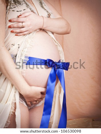 sweet pregnant woman touching her belly with love. Young girl waiting for lovely little baby. Lady in bedroom with tummy and  blue strip belt on it. Pregnancy concept.