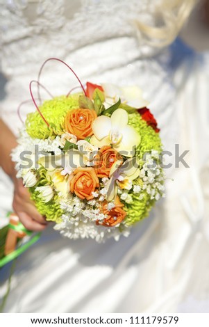 wedding bouquet in hands of bride - woman in white dress holding colorful fresh wedding flowers. Elegant and classic bridal decoration with amazing cream colored orchids and orange roses for marriage