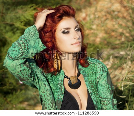 alluring red-haired woman in green oriental shirt posing outdoor. Sexy romantic girl with hand made beads relaxing at nature. Fashion model with professional makeup. Summer-autumn