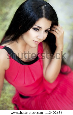 happy young smiling woman posing in autumn park. beautiful girl in stylish red dress relaxing on nature. gorgeous brunette romantic  lady resting and waiting for someone outdoor. positively thinking.