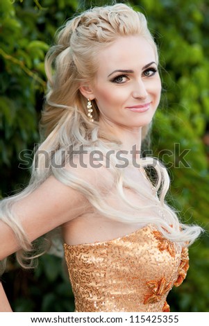 Stylish rich slim girl in sexy golden dress with healthy glossy curly hair in the park. Fashion glamorous shot at vacation resort summer. alluring blond woman in evening dress on nature.Series