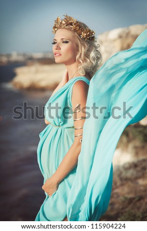 Beautiful pregnant woman outdoor in Greek goddess style with her tummy on sunset  near sea. Young happy girl showing her belly and waiting for little baby. Pregnancy concept. Gorgeous pregnant lady