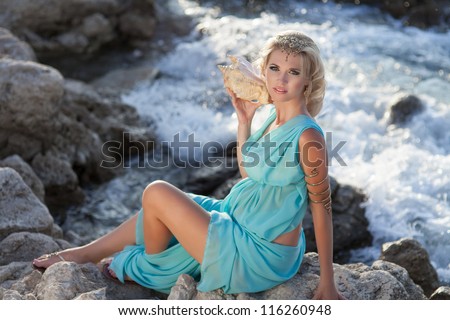 Beautiful pregnant woman outdoor in Greek goddess style with her tummy on sunset near sea. Young happy girl showing her belly and waiting for little baby. Pregnancy concept. Gorgeous pregnant lady