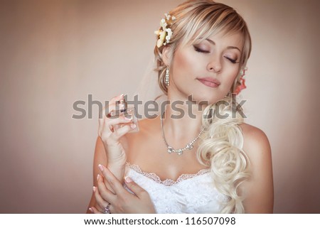Happy sexy beautiful bride blond girl in white wedding dress with hairstyle and bright makeup and perfume bottle. Romantic lady in bridal dress and flowers in hair have final preparation for wedding