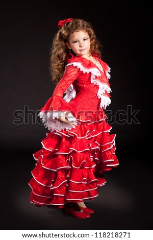 toddler little girl dancing flamenco in traditional spanish red dress. Adorable child from Andalusia with curly hair dancing Gypsy dance. Portrait of artist baby in carnival bellydancing costume.