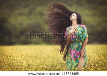 Alluring woman at blossom field with extra long hair on wind. Beautiful  girl in colorful dress posing outdoor. Sexy young lady on nature enjoying freedom. Happy  woman outdoors in autumn park