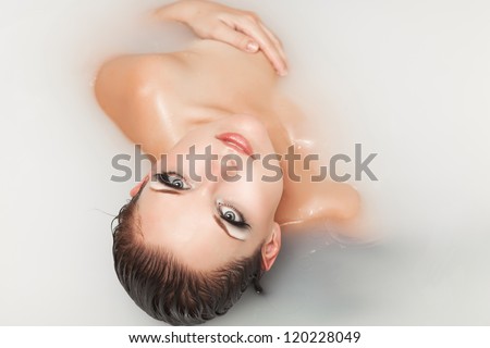 Sexy woman in bath relaxing. Young girl bathing and lying in milk. Alluring brunette posing at bath filled with milk and honey. Model with bright makeup in water. Spa treatments for skin rejuvenation
