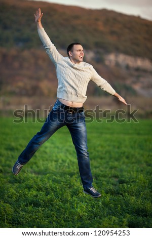 Happy handsome man Enjoying the nature and moment of happiness. Young gue jumping on fresh air in green field. Provence smiling man having fun outdoors at sunset