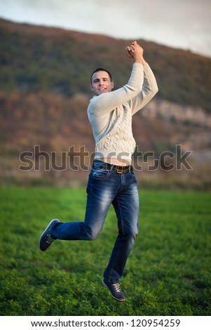 Happy handsome man Enjoying the nature and moment of happiness. Young gue jumping on fresh air in green field. Provence smiling man having fun outdoors at sunset